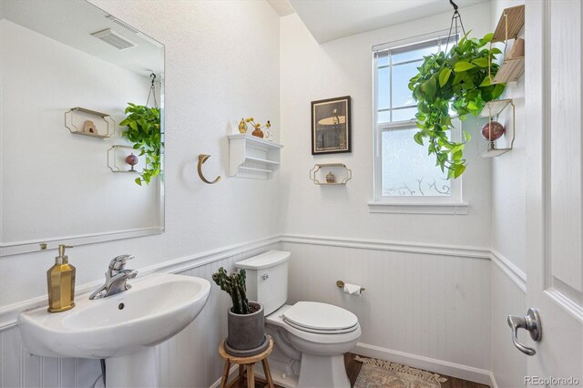 half bath featuring visible vents, a sink, wainscoting, and toilet