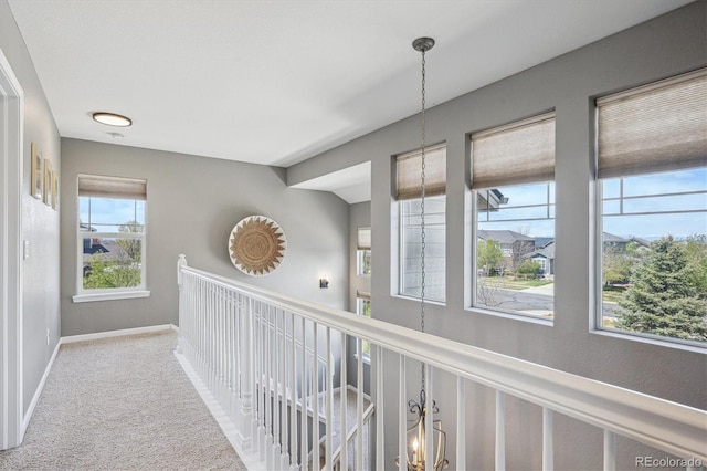 hall featuring carpet flooring, baseboards, and an inviting chandelier