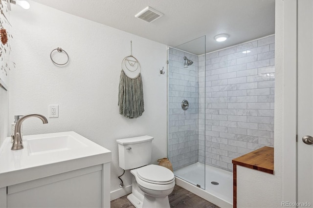 full bathroom with a sink, toilet, wood finished floors, visible vents, and tiled shower