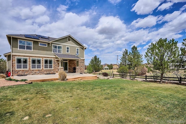 back of property featuring fence, stone siding, board and batten siding, a lawn, and solar panels