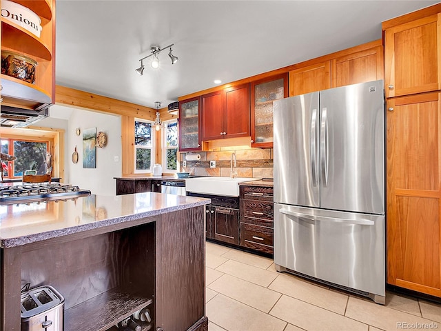 kitchen with glass insert cabinets, light tile patterned floors, light stone counters, appliances with stainless steel finishes, and a sink