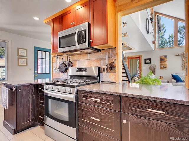 kitchen featuring light tile patterned floors, a peninsula, plenty of natural light, decorative backsplash, and appliances with stainless steel finishes