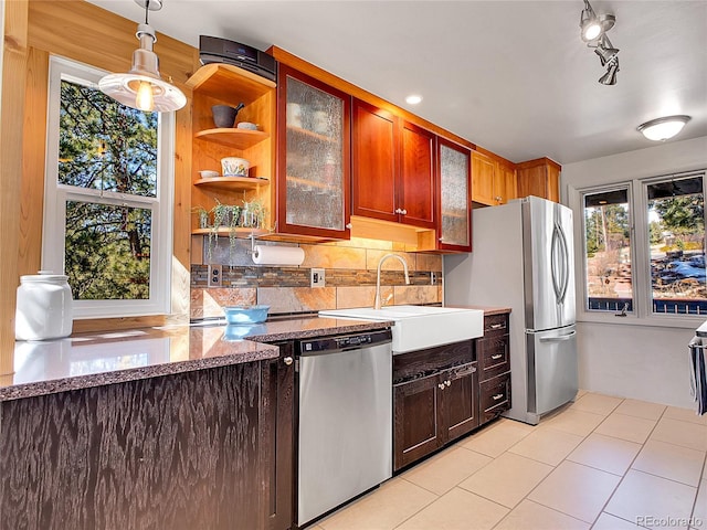 kitchen featuring a sink, backsplash, appliances with stainless steel finishes, light tile patterned flooring, and glass insert cabinets