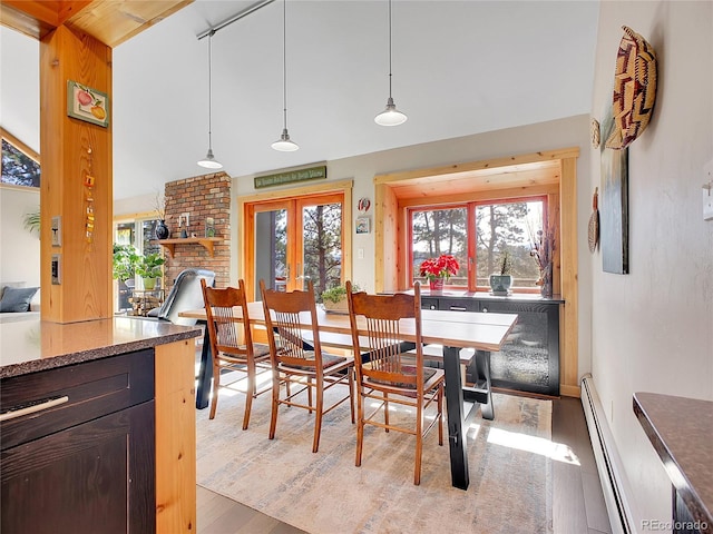 dining area featuring light wood finished floors, a brick fireplace, a baseboard heating unit, french doors, and high vaulted ceiling