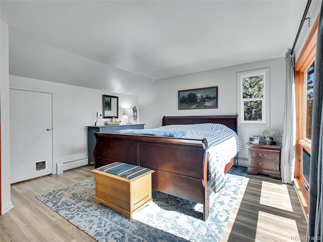 bedroom featuring a baseboard heating unit, vaulted ceiling, light wood-style flooring, and a baseboard radiator