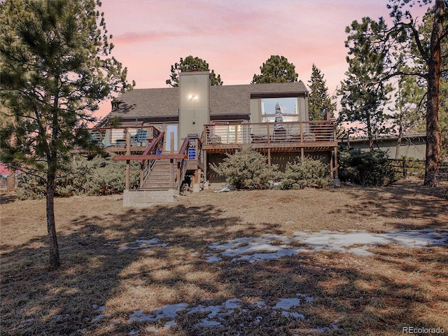 back of property featuring a chimney, a wooden deck, stairs, and a shingled roof