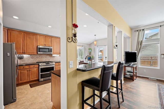 6615 Annanhill Pl, Colorado Springs, CO 80922 - kitchen with stainless steel appliances, dark countertops, a breakfast bar, backsplash, and brown cabinetry