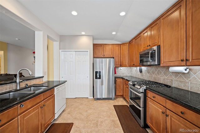 6615 Annanhill Pl, Colorado Springs, CO 80922 - kitchen with appliances with stainless steel finishes, brown cabinetry, backsplash, dark stone counters, and vaulted ceiling
