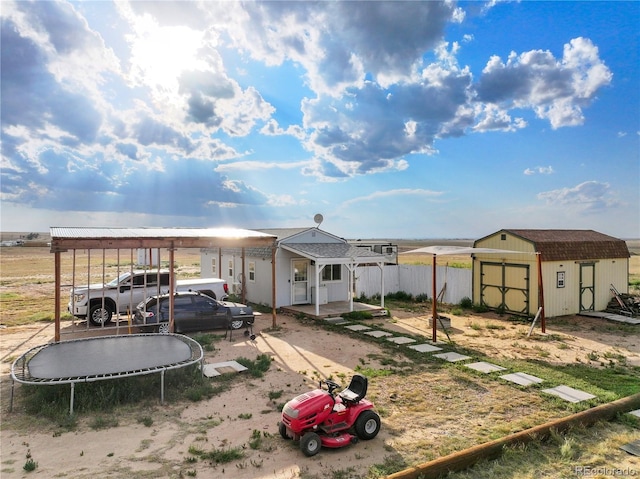 exterior space featuring a trampoline, fence, a shed, a carport, and an outdoor structure