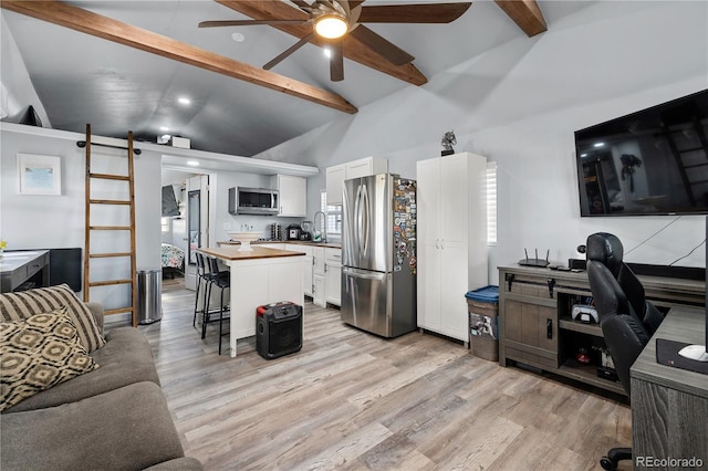 kitchen with white cabinets, appliances with stainless steel finishes, a breakfast bar, open floor plan, and beamed ceiling