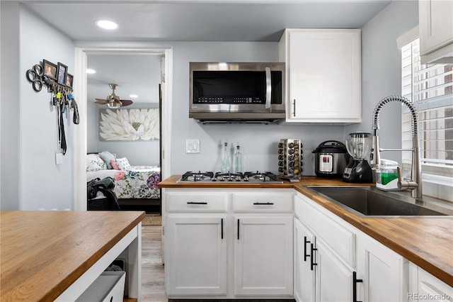 kitchen with a ceiling fan, butcher block counters, stainless steel appliances, white cabinetry, and a sink