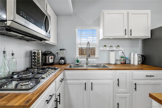 kitchen with white cabinetry, butcher block counters, appliances with stainless steel finishes, and a sink