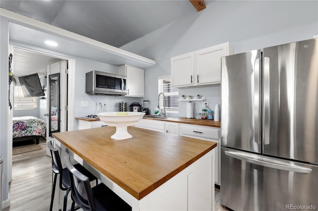 kitchen featuring light wood finished floors, wooden counters, appliances with stainless steel finishes, white cabinetry, and a sink