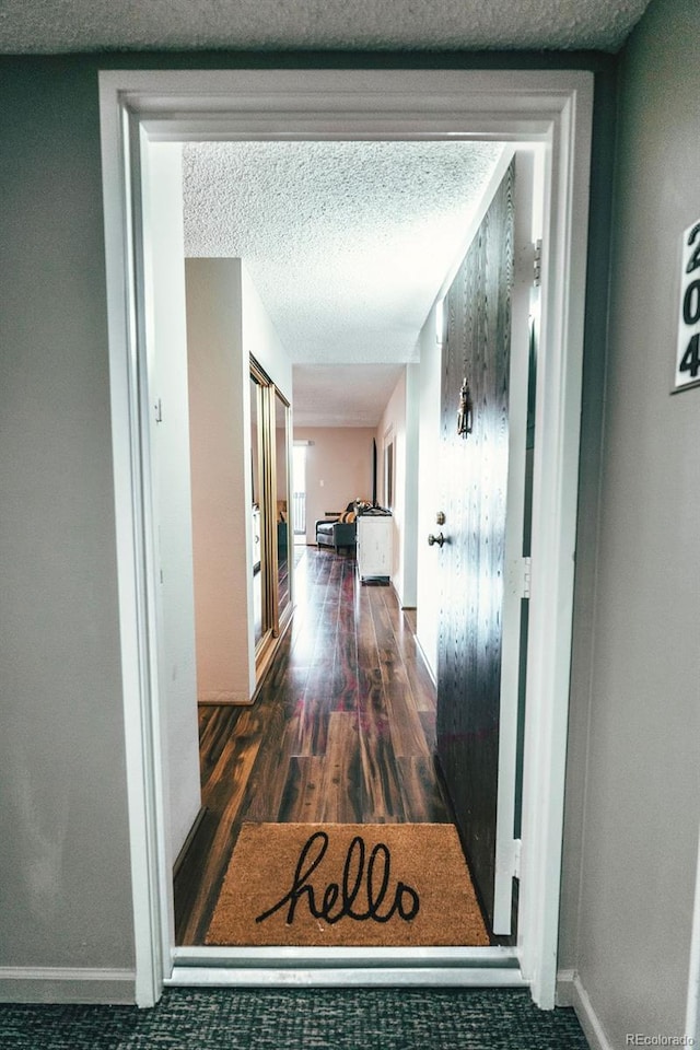 corridor with a textured ceiling, baseboards, and wood finished floors