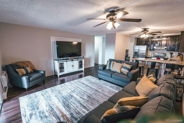 living area with dark wood-style floors, a wall unit AC, ceiling fan, and a textured ceiling