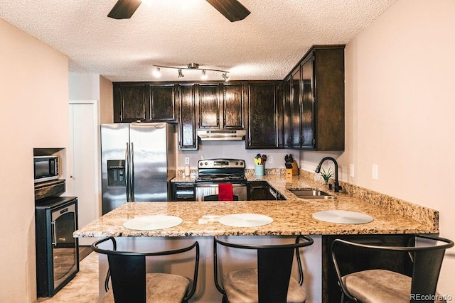 kitchen featuring light stone counters, under cabinet range hood, beverage cooler, a sink, and appliances with stainless steel finishes