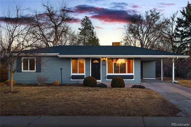 ranch-style house with an attached carport, a yard, driveway, roof with shingles, and a chimney