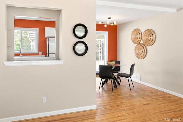 dining area featuring a chandelier, beam ceiling, light wood finished floors, and baseboards