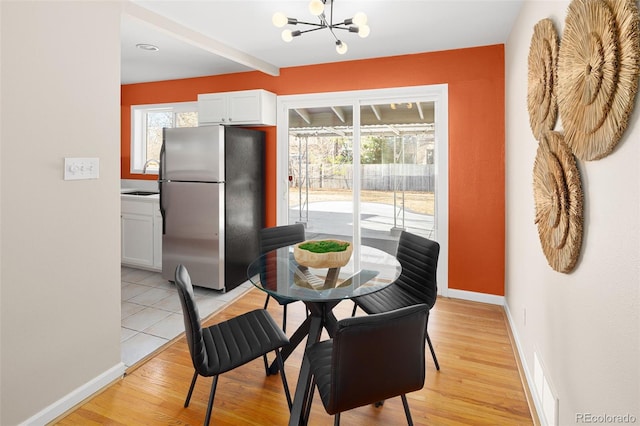 dining space with light wood-type flooring, baseboards, and an inviting chandelier