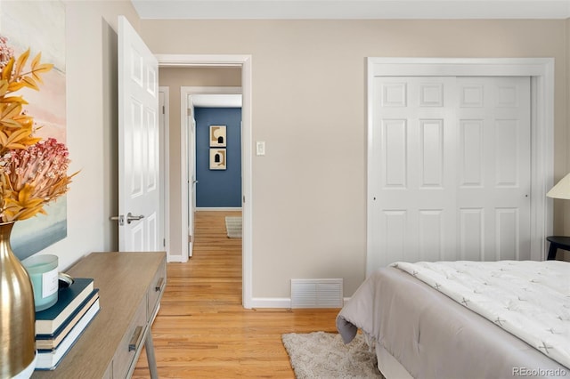 bedroom with light wood finished floors, baseboards, visible vents, and a closet