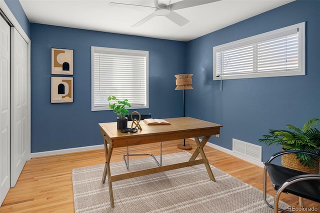 home office with light wood-type flooring, visible vents, ceiling fan, and baseboards