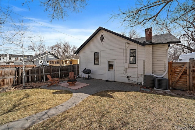 back of property with a chimney, a lawn, a fire pit, a fenced backyard, and a patio