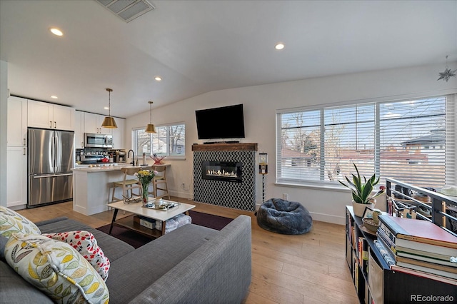 living room featuring a glass covered fireplace, light wood finished floors, baseboards, lofted ceiling, and visible vents