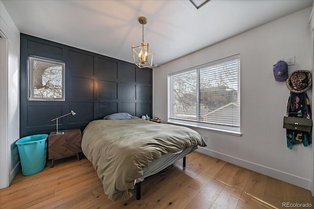 bedroom featuring light wood-type flooring, a decorative wall, baseboards, and an inviting chandelier