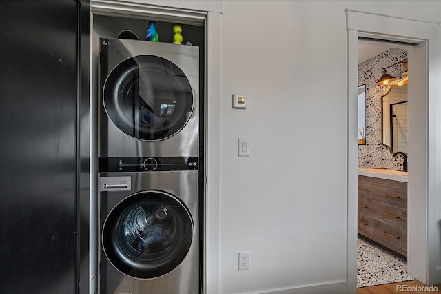 clothes washing area with wood finished floors, stacked washer and clothes dryer, and laundry area