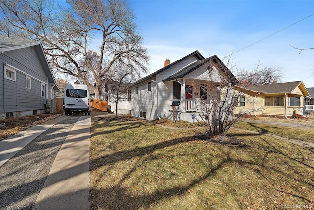 view of side of property with a chimney, covered porch, a yard, and concrete driveway