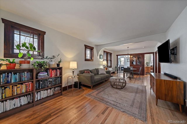 living room featuring baseboards, arched walkways, light wood-style floors, and an inviting chandelier