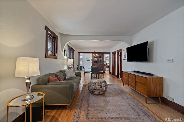 living room with light wood-type flooring, arched walkways, and a chandelier
