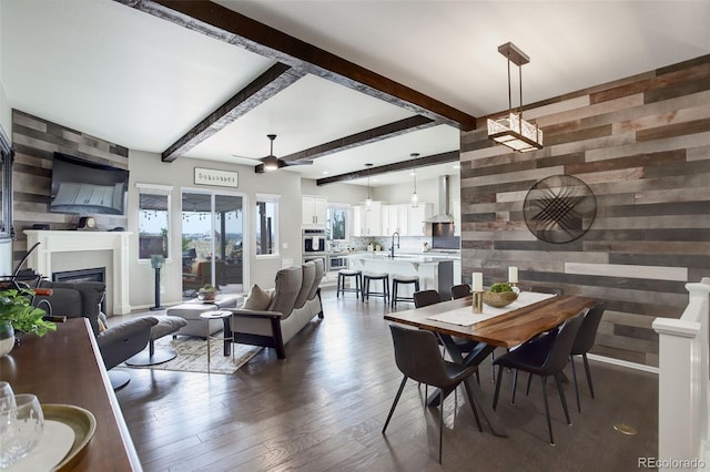 dining space with wood walls, beam ceiling, wood finished floors, and a glass covered fireplace