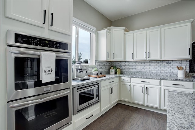 kitchen with light stone counters, white cabinetry, appliances with stainless steel finishes, backsplash, and dark wood finished floors