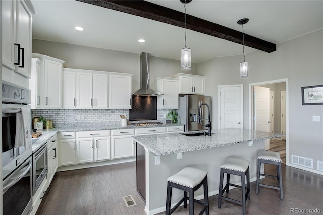 kitchen featuring wall chimney range hood, visible vents, stainless steel appliances, and a sink