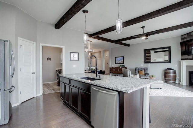 kitchen featuring stainless steel appliances, a glass covered fireplace, open floor plan, a sink, and wood finished floors