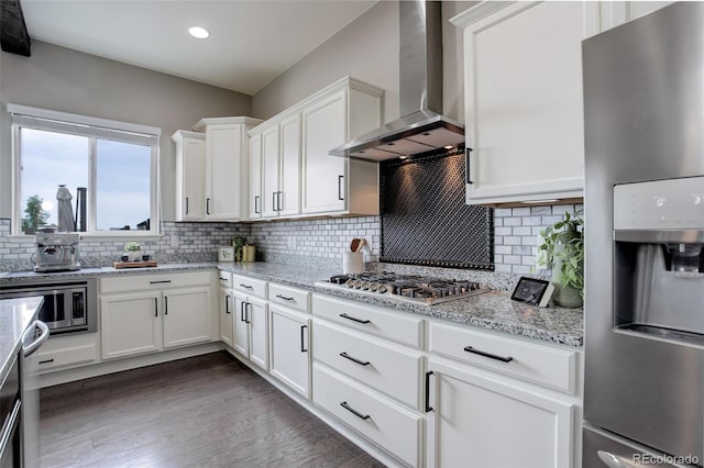 kitchen with stainless steel appliances, decorative backsplash, white cabinetry, wall chimney range hood, and light stone countertops