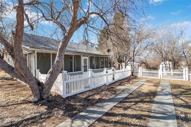 view of side of home featuring a sunroom, a fenced front yard, and a shingled roof