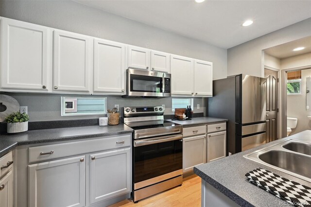 2813 Central Park Blvd, Denver, CO 80238 - kitchen featuring appliances with stainless steel finishes, dark countertops, white cabinetry, light wood finished floors, and recessed lighting