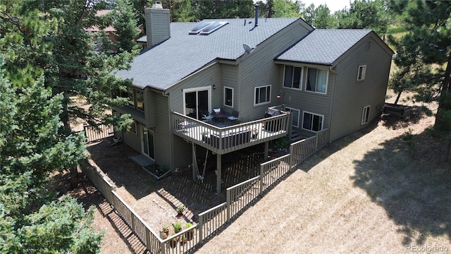 rear view of house featuring a deck, a shingled roof, and a chimney