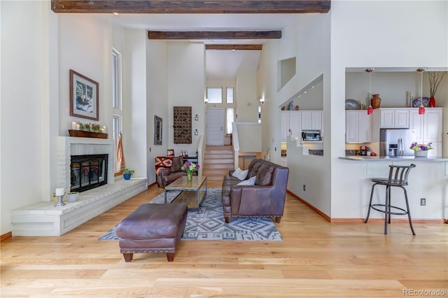 living area featuring a fireplace, light wood-style flooring, a high ceiling, beamed ceiling, and stairs