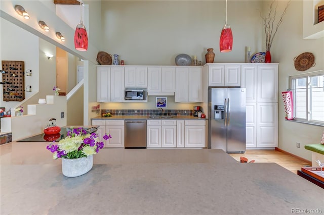 kitchen with a towering ceiling, white cabinets, and stainless steel appliances