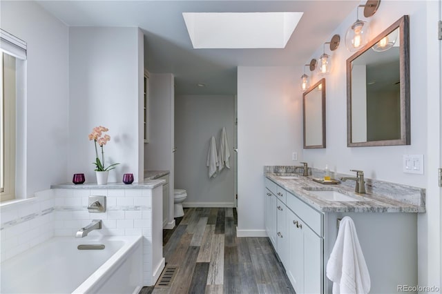 bathroom with a skylight, toilet, wood finished floors, a sink, and a bath