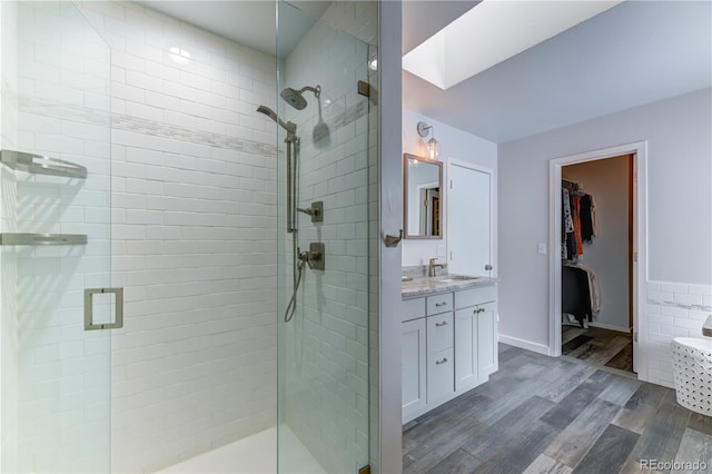 full bath featuring a skylight, wood finished floors, a spacious closet, vanity, and a shower stall