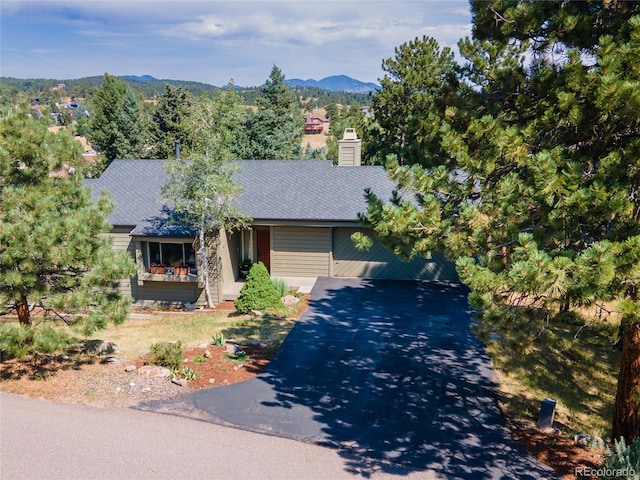 ranch-style home featuring driveway, a shingled roof, a chimney, and a mountain view