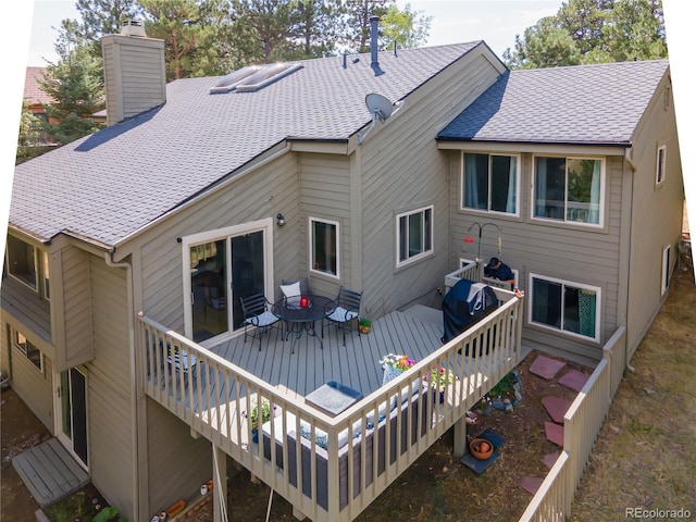 back of house featuring a shingled roof, a chimney, and a wooden deck