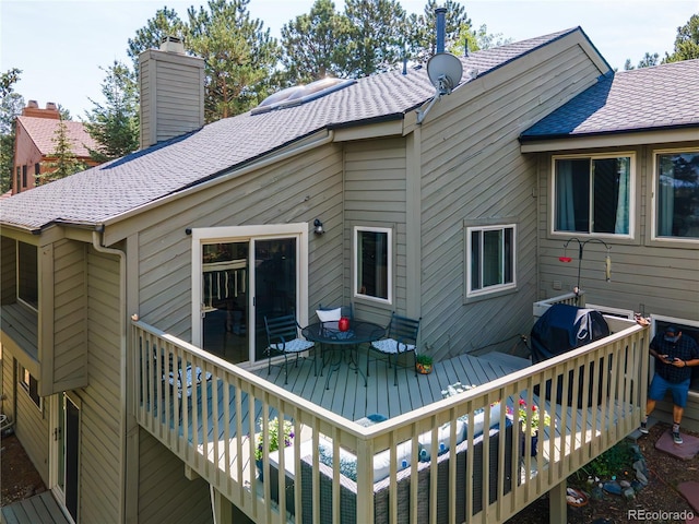 back of house featuring a shingled roof, a chimney, and a wooden deck