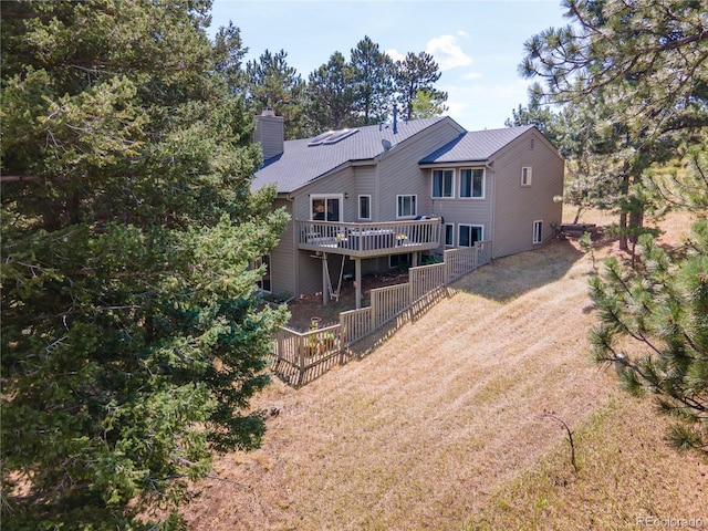 rear view of house with metal roof, dirt driveway, a chimney, and a deck