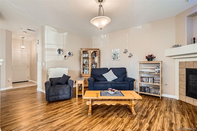 living room featuring visible vents, baseboards, wood finished floors, and a tiled fireplace