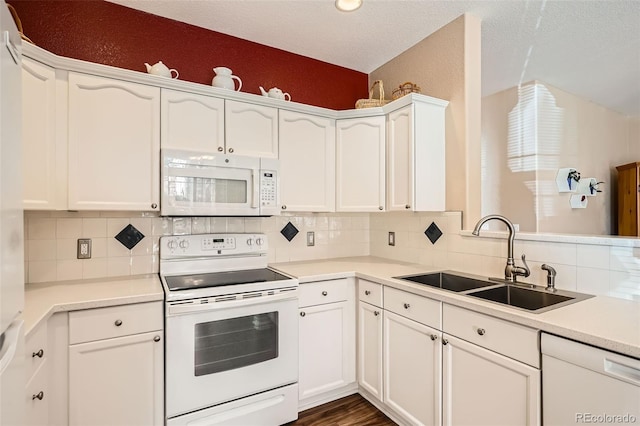 kitchen featuring light countertops, decorative backsplash, white cabinets, white appliances, and a sink